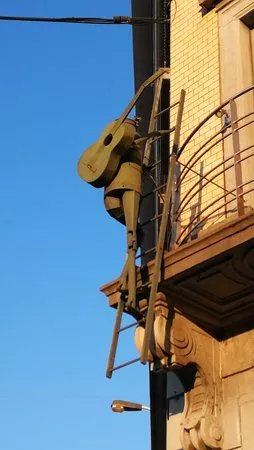 Romeo - Sculpture of a man with a guitar on his back climbing on a ladder
